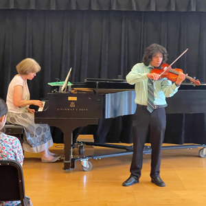 Photo of a male student playing violin with piano accompanist.